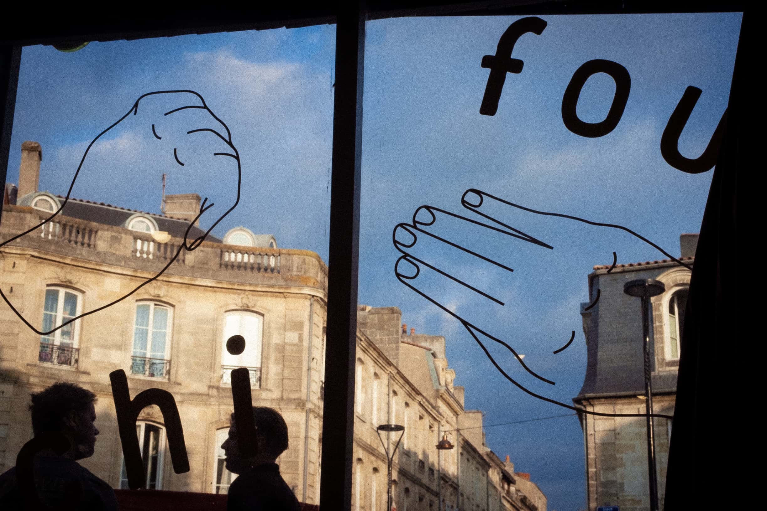 La vitrine du Chifoumi, mains chi fou mi dessinées sur la vitre, façades bordelaises en fond